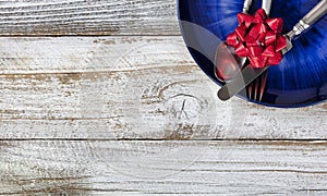 Partial holiday dinner table setting with cutlery and dark blue plate on white rustic wood table