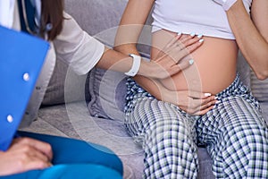 Partial image of female nurse examining belly of pregnant woman in medical room