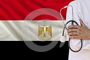 Partial photograph of a doctor with a stethoscope in a professional medical uniform against the background of the national flag of