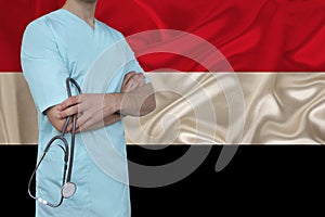 Partial photograph of a male doctor with a stethoscope in uniform against the background of the colored national flag of the state