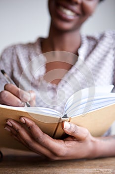 Partial portrait of smiling black female author at home writing in notebook