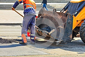 Partial repair of the asphalt road. A worker pours fresh asphalt onto a poor part of the road