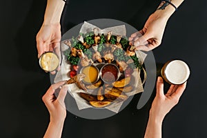 partial top view of people eating baked potatoes with roasted chicken and sauces and drinking beer