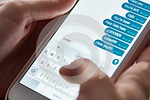 Partial view of abuser sending offensive messages while using smartphone, illustrative editorial.