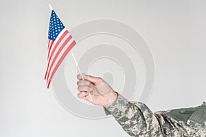 partial view of boy in camouflage clothing holding american flagpole in hand