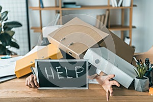 partial view of businessman lying under pile of folders with help blackboard in hands while missing deadlines