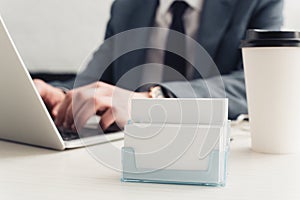 partial view of businessman using laptop near card holder with empty business cards.