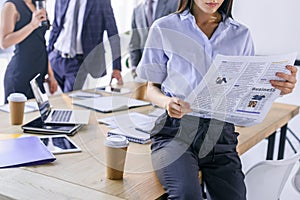partial view of businesswoman reading newspaper and colleagues behind