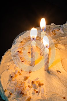 Partial view of cake with cream chesse and coconut frosting with three lighted candels. Celebration concept