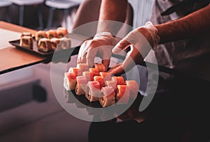 Partial view of chef hand arranging sushi set on slate plate on dark back