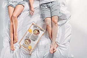 partial view of couple with breakfast on wooden tray resting