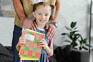 partial view of father and smiling daughter with copybooks in hands at home back to