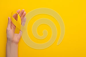 Partial view of female hand with yellow ribbon on colorful background, international childhood cancer day concept . photo