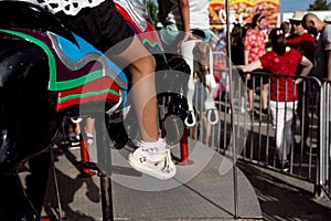 partial view of girls riding merry go round or carrousel during summer on pavement, deep shadows