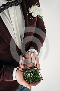 partial view of groom in suit with buttonhole and wedding rings in box