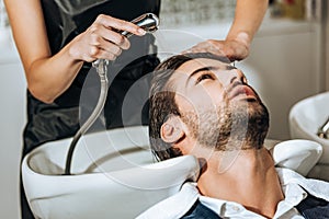 Partial view of hairdresser washing hair to handsome young male client