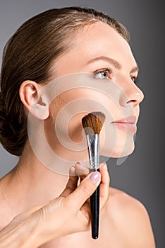 partial view of makeup artist applying blush on models face photo