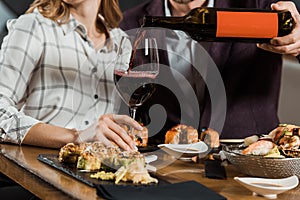 Partial view of man pouring red wine in glass while couple having dinner