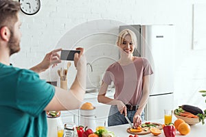 partial view of man taking picture of smiling girlfriend