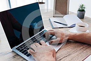 partial view of man typing on laptop at table with coffee cup, textbook, photo frame