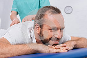 partial view of massage therapist doing massage to smiling patient on massage table