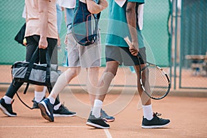 partial view of multicultural elderly men with tennis equipment walking