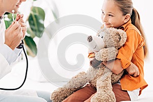 View of pediatrist in white coat and kid with teddy bear in clinic photo
