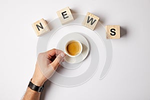 partial view of person with cup of coffee and word news word made of wooden alphabet blocks, on white background