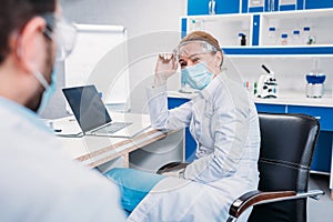 partial view of scientific researchers in white coats at workplace