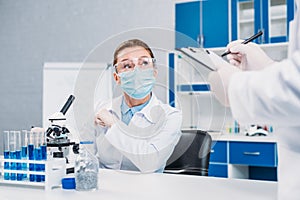 partial view of scientists in medical masks and goggles working on scientific research