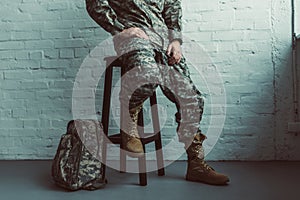 partial view of soldier in military uniform sitting on chair against white