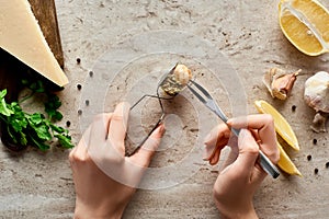 Partial view of woman eating delicious cooked escargots with tweezers on stone background near ingredients.