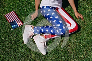 partial view of woman with flagpole in leggins with american flag pattern resting on green lawn, americas independence day