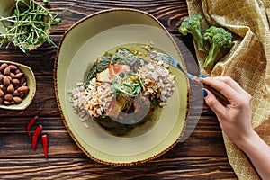 partial view of woman with fork at wooden tabletop with vegetarian salad served with grated almonds