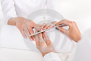 partial view of woman receiving manicure by beautician with nail file at table with towel in beauty salon