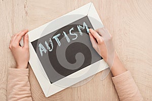 Partial view of woman writing autism lettering with blue chalk on chalkboard.