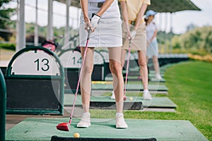 partial view of women with golf clubs playing golf