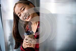 Partial young smiling asian female IT manager with coffee cup looking at camera