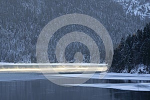 Partially frozen lake plansee with water vapor in the sun-heated ice