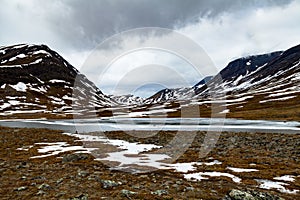 Partially frozen lake in snowy arctic mountains