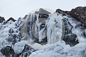 Partially frozen waterfall flows amidst ice formations on a rugged cliffside during a cold winter day