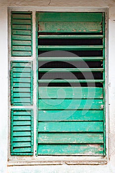 Partially open chipped green shutters in window on white wall