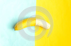 Partially peeled banana on blue yellow background.Tropic summer fruit.
