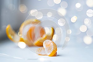 Partially peeled tangerine and tangerine slices, on a light background, with a bokhe of lights.