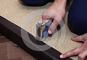 Particle board upholstered with brown leather. Repairman using stapler and staples