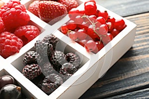 Partitioned box with delicious ripe berries on wooden background