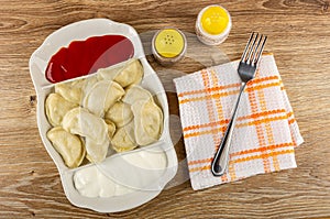 Partitioned dish with dumplings, sour cream and ketchup, pepper and salt, fork on napkin on table. Top view