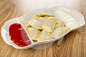 Partitioned dish with dumplings, sour cream and ketchup on table