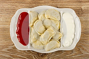 Partitioned dish with dumplings, sour cream and ketchup on table. Top view