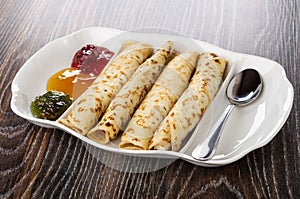 Partitioned dish with jams, pancake rolls, spoon on wooden table